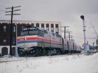 Amtrak 285 leads "The Rainbow" toward the steel arch bridge and the USA in this view from January 28, 1979. The train is seen crossing Queen St. in Niagara Falls. Background building is the King Edward Hotel, also now a part of history. On the right in the far background one can see a revolving tower down in the tourist district.