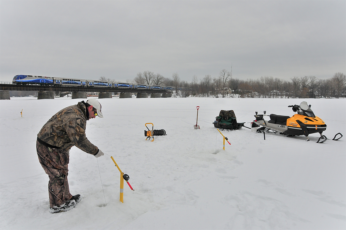 By a cloudy winter day, a fishermen is catching up a pike while AMT #183 is passing over the "Rivière-des-Mille-Îles" with an ALP-45DP in lead.