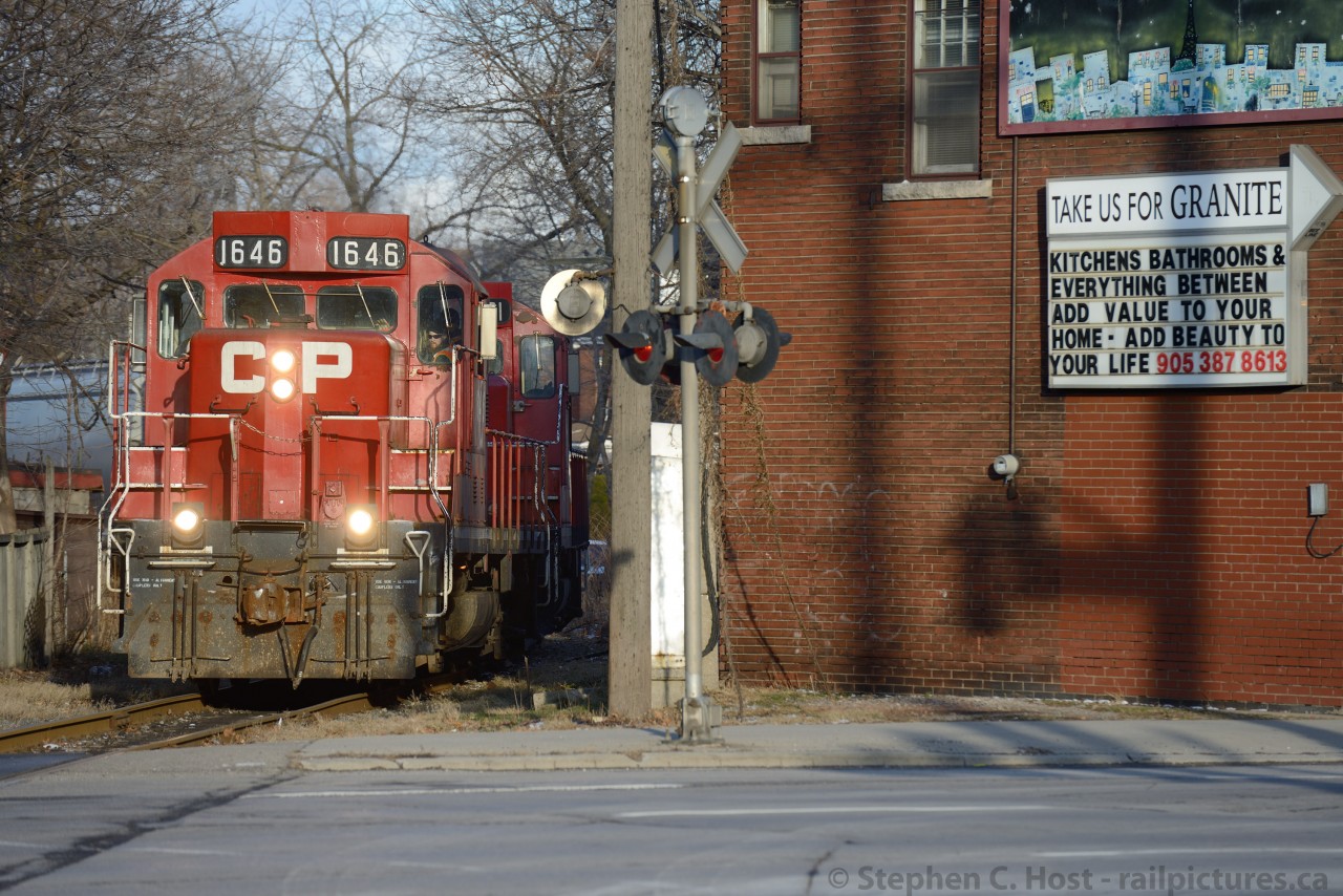 Belt Line:  With the days work nearly completed and Kinnear yard a few hundred feet away we see the Belt Line job emerging between the buildings at Main and Gage St. The train is taking the 'signal' (facing the train) indicating crossing protection is operating normally. The signal displays a white flashing light - and are common throughout the Belt Line having been installed by the TH&B.