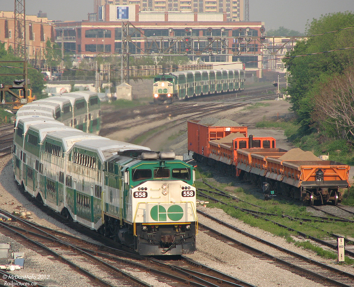 On the home stretch to Toronto, GO Georgetown line train 208 with 558 taking point clatters through the switches at Bathurst Street with a load of sleepy commuters. Following on 208's heels in the distance, GO train 154 with sister F59PH 553 leading,has just entered the Union Station Rail Corridor at Strachan Ave, with a load of commuters off the Milton line.  The orange RFRX ballast cars on the service track on the right were for ongoing rail and switch maintenance work in the corridor at the time. Today (2013) the level crossing at Strachan is almost a memory, as a large trench to grade-separate Strachan has been dug, and the rails have been diverted to the south end of the crossing for its construction. Eventually, the whole corridor will go under Strachan Ave.