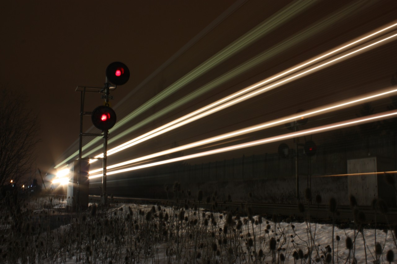 A late night westbound autorack train led by a typical pair of GE GEVOs blurs past the signals at Lisgar and is about to get caught by the hot box detector.