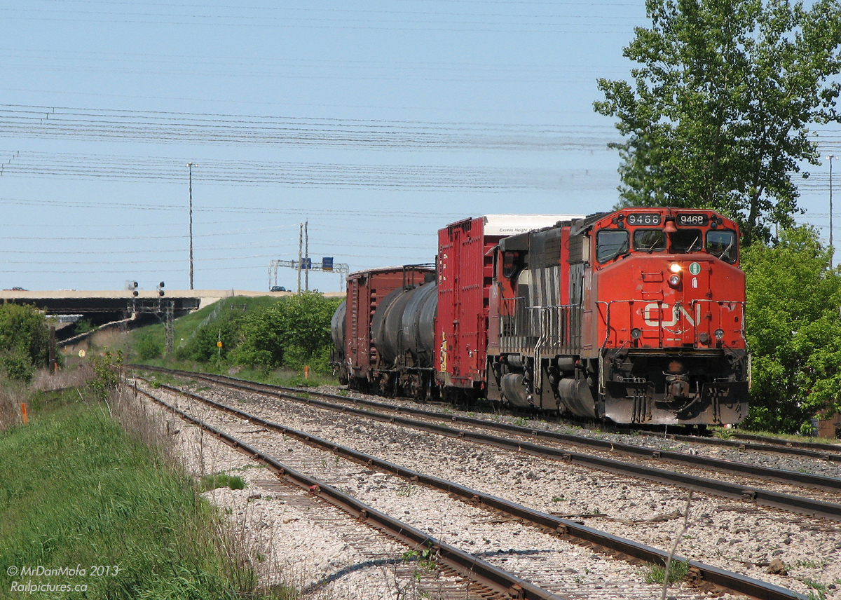 Like shooting fish in a barrel.After running out of batteries standing trackside just as CN #577 departed Malport Yard (about a kilometre up the road), I quickly swapped in some new ones and zipped down Torbram Road to catch them at the crossing just to the south. A pair of CN GP40-2L(W) units, rare to find on the mainline but the soup du jour of 577, haul their train around the bend from the Halton Sub onto the Weston via the low speed north service track on a hazy spring morning. The junction point of Halwest (officially by Hwy 407 on the left in the distance, in Brampton) is the meeting point between the busy Halton Sub mainline from Burlington to Vaughan, and the mostly passenger Weston Sub from Toronto to Brampton (where we are right now was taken just across the city limits in Mississauga). 577 was at the time the regular CN-CP interchange train, taking CP cars to West Toronto/The Junction and CN cars back to MacMillan Yard in Vaughan.