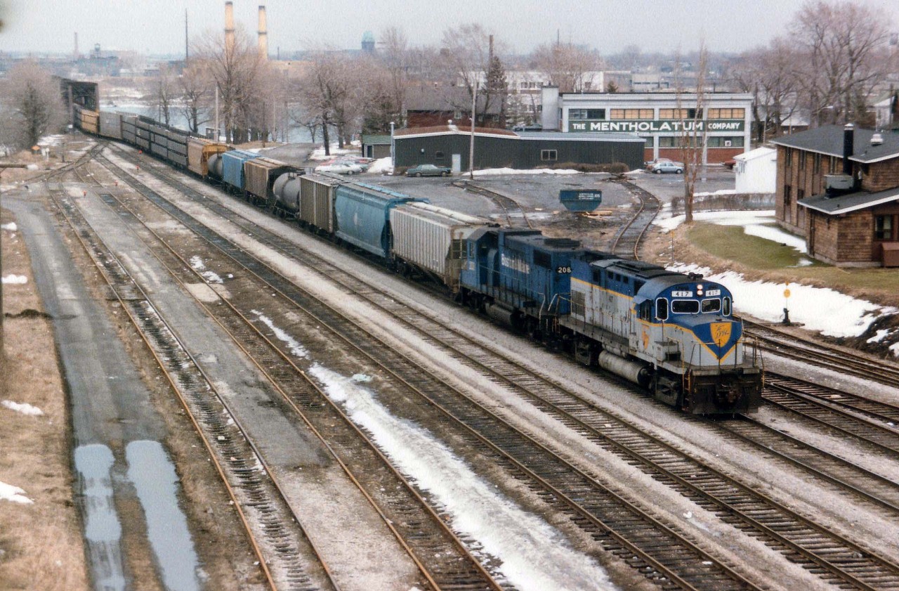 To those of us who wander thru the remnants at Fort Erie CN yard in search of what used to be, this scene is a bit hard to swallow. Look at all the trackage!!!  In this view, D&H 417 and B&M 208 are seen bringing over the daily transfer from Buffalo. One can see the old CN Crew Hostel in the background at right, as well as a couple of stubs behind what used to be a station site; on this track there sometimes were freight cars marked "BOEING" which were left for an aeroplane parts company located up the street. Photo from the Central Avenue bridge now not doable on account numerous thick hydro lines marring the view.