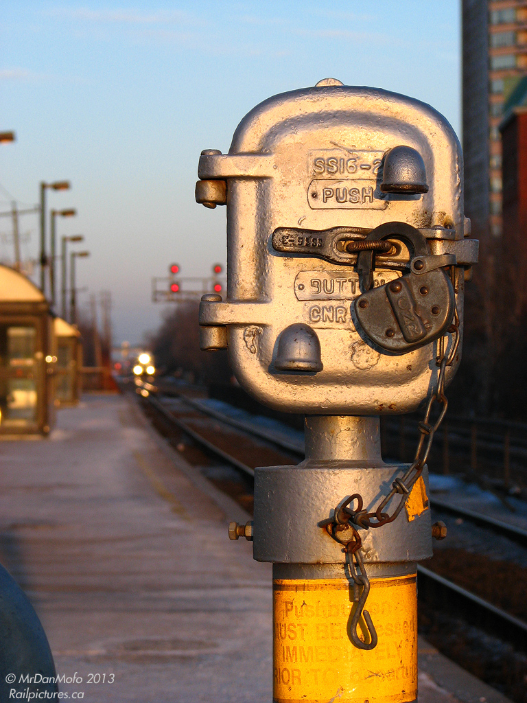 With the next evening GO train speeding towards the station in the distance, the switch lock on Brampton Station's push-button crossing activation box sits loosely fixed, awaiting the eventual push of GO #207's conductor. Used for reactivating the nearby crossing after the circuit detection system turns it off during prolonged station stops, today the push buttons are gone and replaced with radio signal activation via keying a code into the radio; another vanished analogue relic replaced by modern computers and digital radio signals.