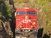 A little over a mile to the west of the Kenora station the double track mainline splits with the south track boring straight through a rock knoll and the north track curving around it. Eastbound train cp110 running today with ES44AC CP8774 as the rear remote is about to pass through this short tunnel highlited with spring greenery. 