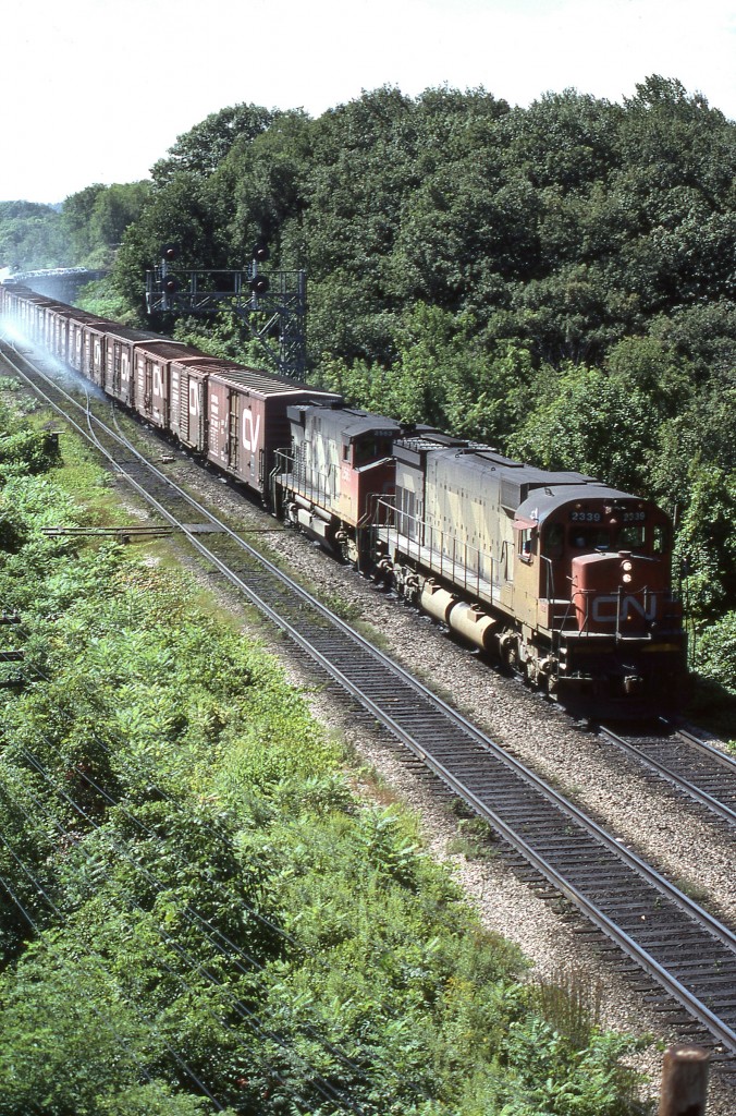 Last of class Canadian National M-636 2339 powers past Bayview Jct. accompanied by MLW cousin M-420(W) 2563. During 1970, 1971 CN acquired a total of forty (Nos. 2300 -2339) of MLW’s highest horsepower production six motor locomotive.  No. 2339 would soldier on until 1995 and be retired. Hope there are no rolled down windows in the open style autoracks. If so, the salesman will have a difficult time explaining why the new car smell has been replaced by the smell of brake shoes!