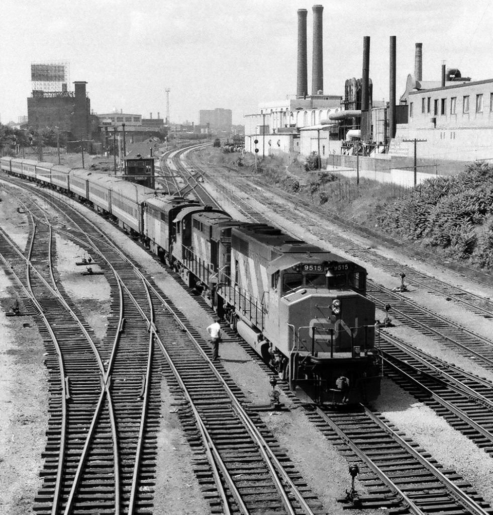 The westerly view from the Bathurst Street bridge. Worth modeling: The trackwork; Manually operated mainline switches; Cabin D operational; CN GP40 in passenger service; Conventional coaches, one still in CN b & w. And the background  smoke stacks from Toronto's industrial age....the whole image is another age !


The Toronto Terminals Railway switch tender keeps a keen eye on 9515's running gear, accompanied by a CN 3100 (RS-10) and a FPA-4,  as VIA Rail # 74 rolls through the multiple Bathurst Street turnouts. (  GMD built 9515 delivered to CN in 1974 ). September 1979 negative by S.Danko.

More at Bathurst Street:


  westbound CP Rail   


  Tempo  


  CP Rail #11