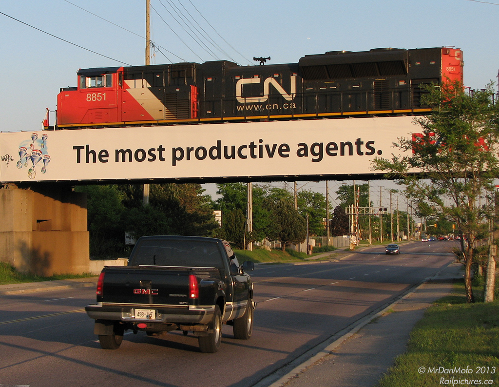 GM over GM<
br>
Rumbling over traffic (including a GMC pickup truck) on the busy Islington Avenue below, CN #115 with 8851 on point heads east after departing Brampton Intermodal Terminal and crossing the massive Humber River bridge (Mile 4.3 of the Halton Sub). Skirting the north side of Toronto just north of Steeles Ave, a stone's throw away one can note CP's MacTier Subdivision crossing just north of the Emery industrial area.

Built by Electro Motive's General Motors Diesel Division in London ON, SD70M-2 8851 was as good as it got in terms of new power on CN at the time. Alas, with the Caterpillar takeover and elimination of the London plant they're no longer made with Canadian pride, instead in work-to-rule Muncie, Indiana at lower wages. A sign of the times.