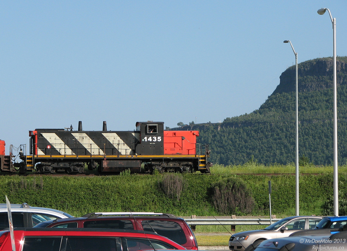 Rolling past the towering Mount MaKay in the background and the Thunder Bay International Airport in the foreground, CN GMD1 1435 rolls by automobiles not even 1/4 of her age on a crosstown grain transfer, from Port Arthur to the Neebing area.