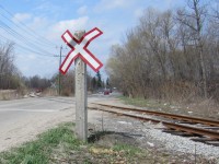 X (and a rock) marks the Spot. New signals are on the way for the BCRY crossings of Huronia Road in Barrie. This long serving wood post with it's nailed on aluminum numbers will soon be a thing of the past. In the background the tracks get a little spring maintenance.