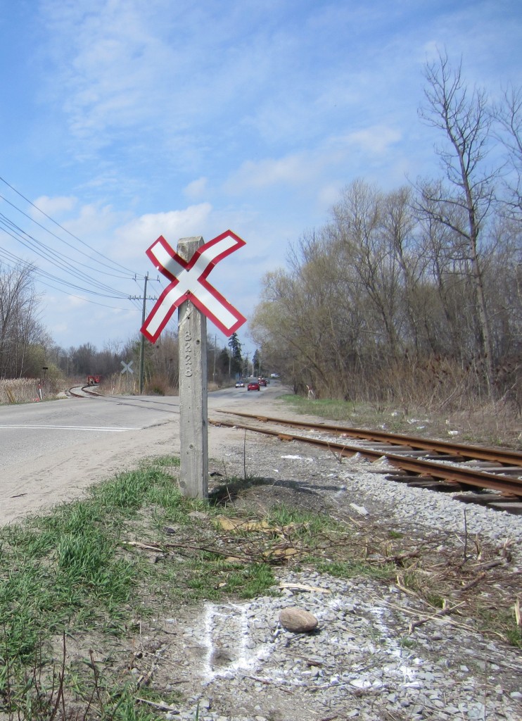 X (and a rock) marks the Spot. New signals are on the way for the BCRY crossings of Huronia Road in Barrie. This long serving wood post with it's nailed on aluminum numbers will soon be a thing of the past. In the background the tracks get a little spring maintenance.