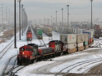 Working the north end of the busy Brampton Intermodal Terminal, CN's main Ontario intermodal facility, yard Geep 7246, slug 257 and road Geep 4108 shuffle around well cars and containers into trains bound for all points across North America. In the background, piggypackers and container cranes can be seen loading and unloading containers between trucks and railcars that 7246's set spots.  <br><br>Just behind the power, CN intermodal train #114 with recently repainted Dash-8M 2434 and a BC Rail sister is seen arriving and waiting to pull ahead, with more containers to unload.  <br><br>If it looks cold, it was: winter's grasp had not left in this February shot, and it was a very cold few minutes spend on the top of the windy Highway 7 overpass to catch the action.