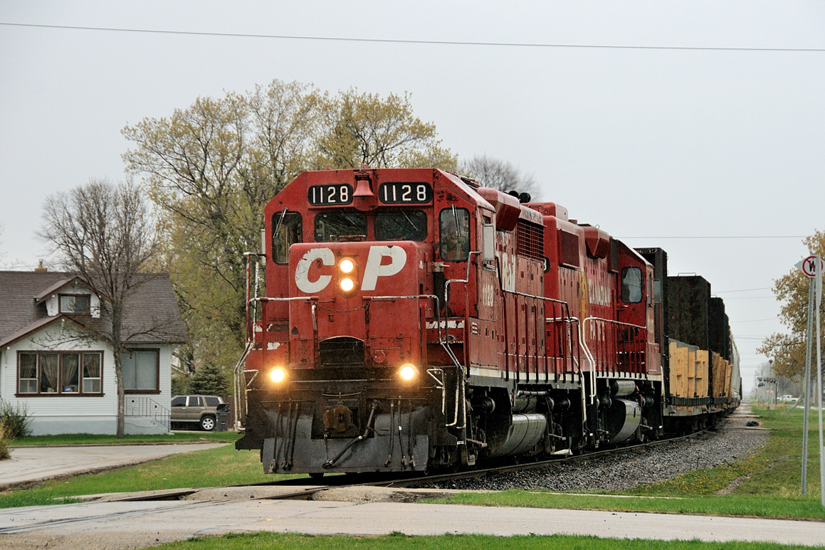 "The Selkirk" trundles through residential suburbia as the train makes its thrice weekly trip down the Winnipeg Beach Sub with steel traffic from Selkirk and traffic from the Lake Line Railway, who operates the northern portion of the Sub from Selkirk to Gimli. Today's 17 car train is on approach to the gateway into Winnipeg Yard: Rugby Interlocking. The crew has got the okay from the Supervisor Operations Terminal (SOT)to enter the Arborg Sub (a handthrow switch just west of Rugby) and a track on the east side of Rugby to put their train away.