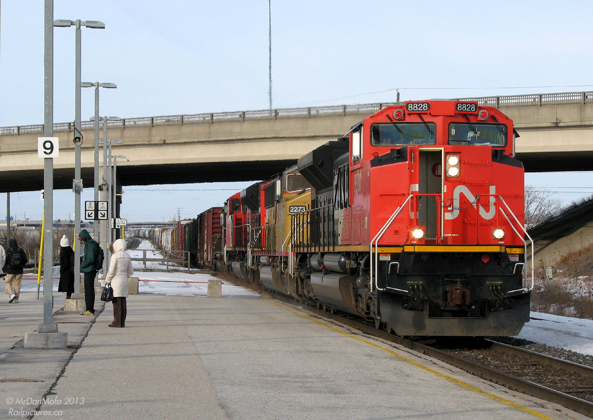 Right Time, Wrong Train.  Creatures of habit, early morning commuters await the arrival of their Toronto-bound GO train, "the 8:08 from Bramalea" (formally known as train #210 from Georgetown), on the middle platform, on the south track, just as they do every morning. Except today, things are a little different. It's now 8:14am and the usual GO that was supposed to arrive 6 minutes ago is a no-show, replaced by a long CN freight train rumbling through on the opposite side of the platform.   Yup, you guessed it: the CN Rail Traffic Controller, for whatever reason, held the GO at Brampton and ran this monster of a CN #394 ahead on the single track section. Motoring east on the north track with 15,400 horsepower on the head end, shiny CN SD70M-2's 8828 & 8840, yellow UP SD60M 2273, and black IC 6050 muscle their train eastward to Concord, while anxious commuters peer down the track looking for the headlight of their GO train. After the tail end of the freight clears, the GO will get the green light, and arrive at Bramalea 10 minutes late to pick everyone up.  It's business as usual on the railway, and just another day taking the GO into The Big Smoke.