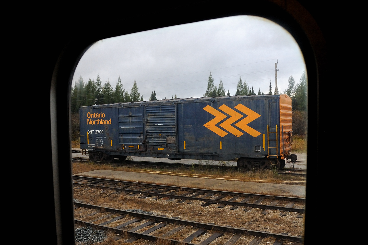 Seen through the vestibule window from the Polar Bear Express, Ontario Northland boxcar 2709 sits on one of the shop tracks in front of the old engine shed across from the station on a gloomy day in far, northeastern Ontario.