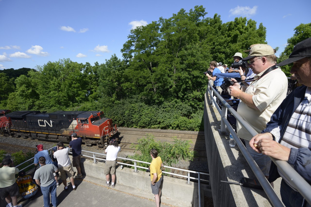 The froth runs strong as the crowd attending the 18th annual Bayview Meet watch as an eastbound passes under the bridge.
The 19th annual CNET Bayview Meet occurs on Saturday June 22 2013 at the Royal Botanical Gardens  Laking Garden pedestrian bridge. Come out and meet many of the people who visit, contribute to and run Railpictures.ca. Everyone is welcome, and an award (in spirit) is offered to those that come from furthest away to the event.
For anyone new - the first group of people usually show up for 0500 and stay most of the daylight hours. Be sure to sign the guestbook when you arrive. Some brave souls pull a 24 hour event starting at 0001 and  log all trains that pass. Parking is free and no admission is required unless you plan to enter the RBG. Washrooms and water facilities are available just across the bridge. There is a traditional lunchtime BBQ - it would be appreciated if you could bring sides/snacks for BBQ or extra drinks and water. Otherwise, there is lots of food and coffee a few KM east on Plains Rd in Burlington.
