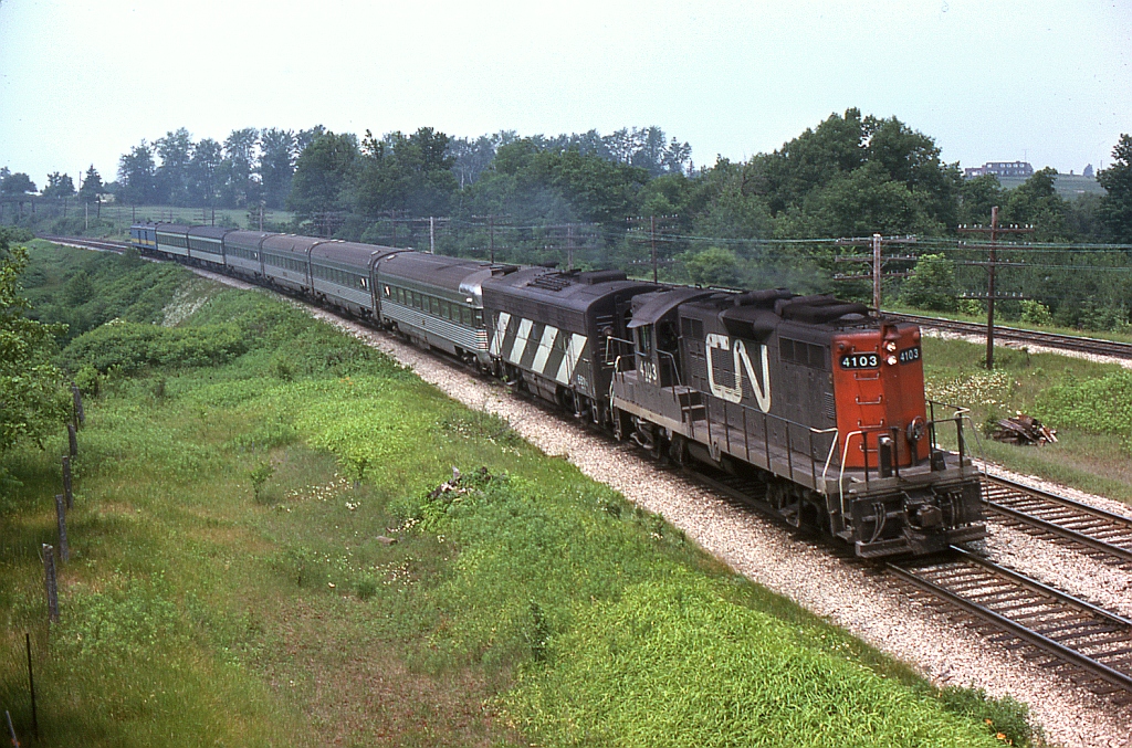 CP is well known for operating their stainless steel passenger cars across Canada, but CN also had a few of their own as well: in 1962 CN purchased a set of stainless steel Budd passenger cars from the Reading Railroad, previously used on their "Crusader" train. The cars consisting of the full 5 car consist of two coaches, a diner, and two observation cars (the idea was to have an observation at either end to be able to run around the train, rather than wye or turn it). Once refurbished and branded under the "Champlain" name, the set was initially used in service between Montreal and Quebec City, but later appeared on some of the southern Ontario corridor trains. There was also a regular CN baggage car painted black and silver to match this consist (not shown here). The five cars (300-304) survived into the VIA era until retired in 1982, although they never did wear VIA blue. Three of the cars were sold for scrap, but the observations were resold and survive in the US: one at a museum and another on a dinner train.  Here we see CN "VIA" 74 with GP9 4103 leading an F9B, 4 of the 5 Crusader cars (including an observation), and some regular steel CN & VIA cars at Hyde Park, just east of Denfield Road near London Ontario. Instead of wying the train at the end of its run, CN often just wyed or ran the power around and pulled the train back from the other end, hence the observation car right behind the B-unit and the baggage car trailing.  Not factoring in the hoard of self-propelled CN RDC units, the former Crusader passenger cars made for an interesting glimmer in the sea of CN white and red (and later VIA blue and yellow).