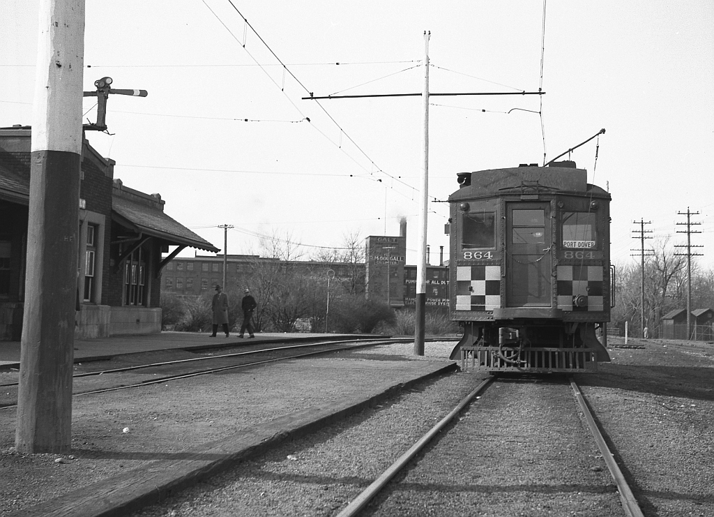 An end view of Grand River Railway electric passenger car 864, sitting outside the GRR - LE&N Galt Main Street Station (not to be confused with the CPR's own Galt Station to the north). The Galt Main Street Station was mile zero for both the LE&N and the GRR. The photo is looking north, 864 is facing north on the southbound track, and the light angle would make this a late morning photo. The car is likely off a LE&N Train north from Port Dover, train #5 to Kitchener.    In the background is the McDougall Foundry, a long-gone casting firm. CN's Fergus sub is barely visible to the right of the photo.  Photo taken by Cecil Hommerding, from the collection (Copyright) of Doug Leffler. Substantial caption information provided by George Roth et al with much thanks.  Other station photos: The GRR - LE&N Station itself: http://www.railpictures.ca/?attachment_id=10502  A better view of GRR car 864: http://www.railpictures.ca/?attachment_id=10474  The fantrip stopping off at Kitchener Station: http://www.railpictures.ca/?attachment_id=10681  For more details on Cecil, see here.