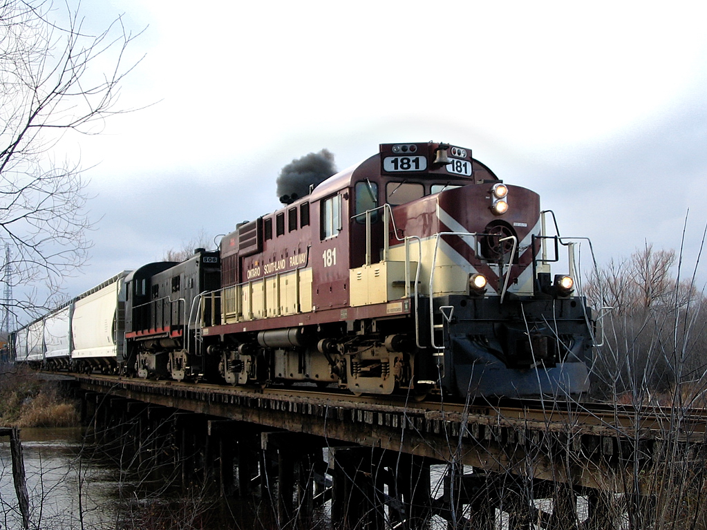 The early days of a hobby. I'm 17, have a G2 license and access to my parents 1999 Honda Civic and their basic point and shoot camera, a Canon Powershot A75. What turned out to be a Friday ritual (parents permision or not!), on my spare period at Centre Wellington District H.S. in Fergus, take the camera and Civic down to Guelph to catch the afternoon activity, normally focusing on OSR and hopefully catching a late GEXR 580 depart Guelph or catching GEXR 431 returning from Mac Yard to Stratford. 
One of my first experiences I caught OSR returning through downtown from the interchange (with GEXR), with RS18u 181 and RS23 506. They had some work at Polymer Distribution Inc. (PDI) yard before they departed for Guelph Jct at Campbellville, Ont. I made my way south to the wooden trestle over the Eramosa River and waited over an hour for them to finish their work. In my mind at the time, it was a thing of beauty. The sun peaking out of the clouds making the colour of the maroon and beige engine standing out against the grey November sky, and the engineer throttling up showcasing the trademark MLW "smoke show". 8 years later it is still one of my favourite photo's, however the unsightly twigs around the nose make me cringe everytime I look back on this image...