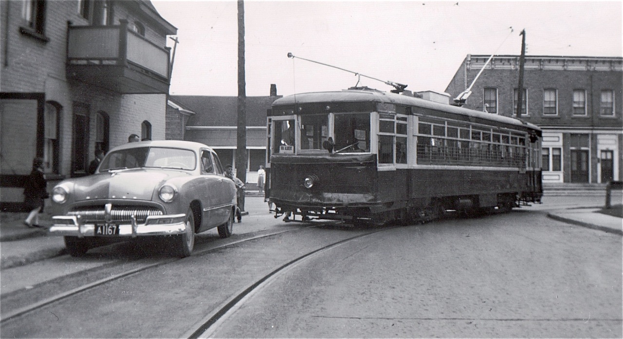 Street car operations in Cornwall ended in July 1949 and most passenger carrying equipment was scrapped shortly thereafter.  This car, 29, which had started its working life in Fort Worth, Texas and arrived in Cornwall in 1939, survived somewhat longer and was made available by a cooperative management for fantrips over the remaining and still extensive network of track, with electric overhead intact, devoted to the CSR’s freight operations.  This scene illustrates one of the risks of operating such an excursion on a Sunday when freight movements normally took the day off.  After some delay the impasse was resolved and 29 completed its left turn from Marlborough Street onto William Street.