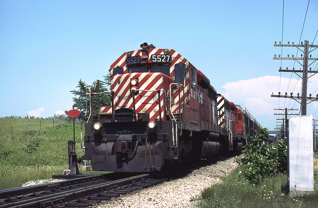 A pair of SD40's with CP 5527 in the lead head westbound by the east siding switch of Lobo, on the CP Windsor Sub west of Denfield Road bridge.