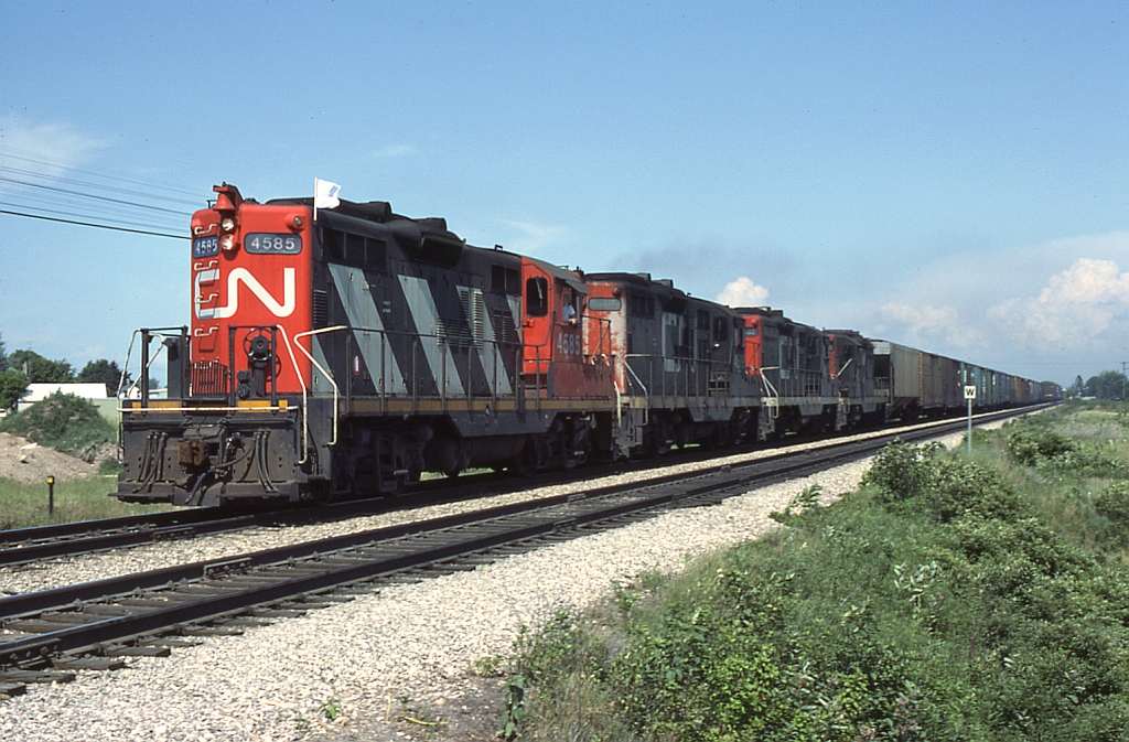 With a lone white flag flapping away, CN 4585 leads a nice four-pack of GMD GP9's hauling an extra freight through Hyde Park. The trailing 3 units are still in the CN noodle scheme (red ends, black carbody, white frame, big CN on hood sides), compared to the 4585 in the newer "zebra" livery featuring red ends, nose and cab, yellow reflective frame striping, CN noodles at the ends and white carbody striping along the hood sides.

* Exact location unknown, possibly westbound at Hyde Park Road grade crossing.