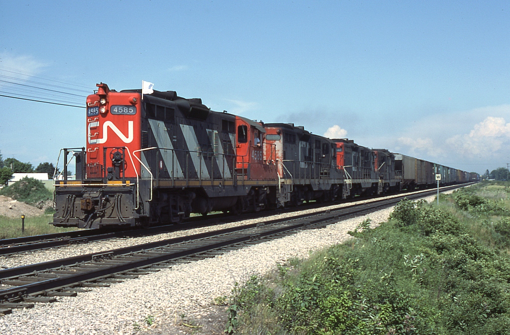 With a lone white flag flapping away, CN 4585 leads a nice four-pack of GMD GP9's hauling an extra freight through Hyde Park. The trailing 3 units are still in the CN noodle scheme (red ends, black carbody, white frame, big CN on hood sides), compared to the 4585 in the newer "zebra" livery featuring red ends, nose and cab, yellow reflective frame striping, CN noodles at the ends and white carbody striping along the hood sides.

* Exact location unknown, possibly westbound at Hyde Park Road grade crossing.