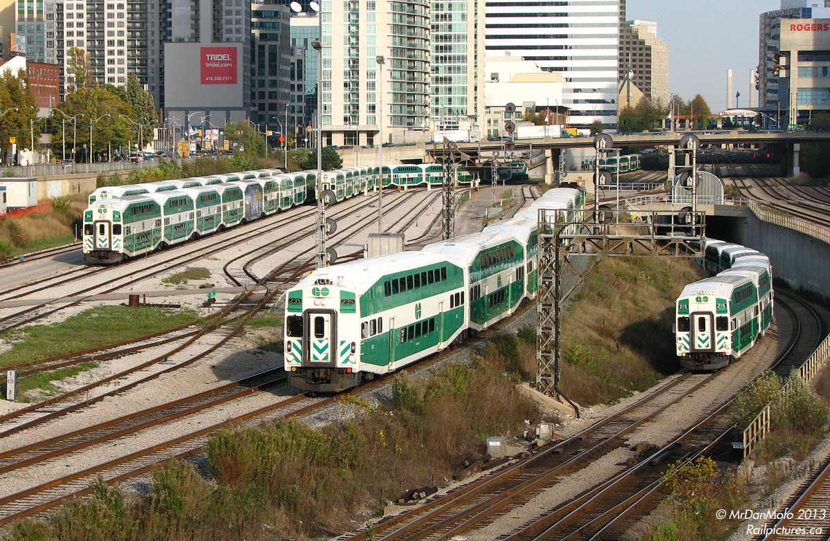 Commuter Chaos. At the height of evening rush hour, GO trains are coming and going every which way out of Union Station. At Bathurst Street, GO cab car 235 leads the first evening Bradford line (not extended to Barrie yet) train, #801, out of downtown Toronto on its way to Parkdale and up the Newmarket Sub. GO 215 leads Lakeshore West train #479 out of the Flyunder, destined for Mississauga, Oakville and Burlington. On the left, Bathurst North Yard is emptying as trains that have laid over the afternoon depart for Union Station, where they will load weary commuters heading home north, west and east of Toronto.