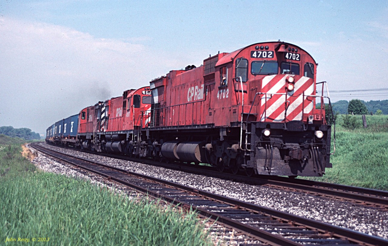 M-636 #4702 leads an M-630 and an RS-18 east on hot container train 502 at Lovekin siding, Belleville sub in August 1990.