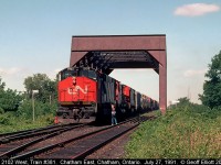 CN HR616 #2102 has train #381 down to a crawl as it readies to negotiate the cross-overs at Chatham East on July 27, 1991.  The Chatham East Operator has hoop and orders in hand as the Brakeman on 381 leans down to snag them.  2102 will go through the cross-overs and diverge onto the CSX Sarnia Sub for it's short run to Fargo, where the train will again turn west onto the CASO to finish out it's run to Windsor.