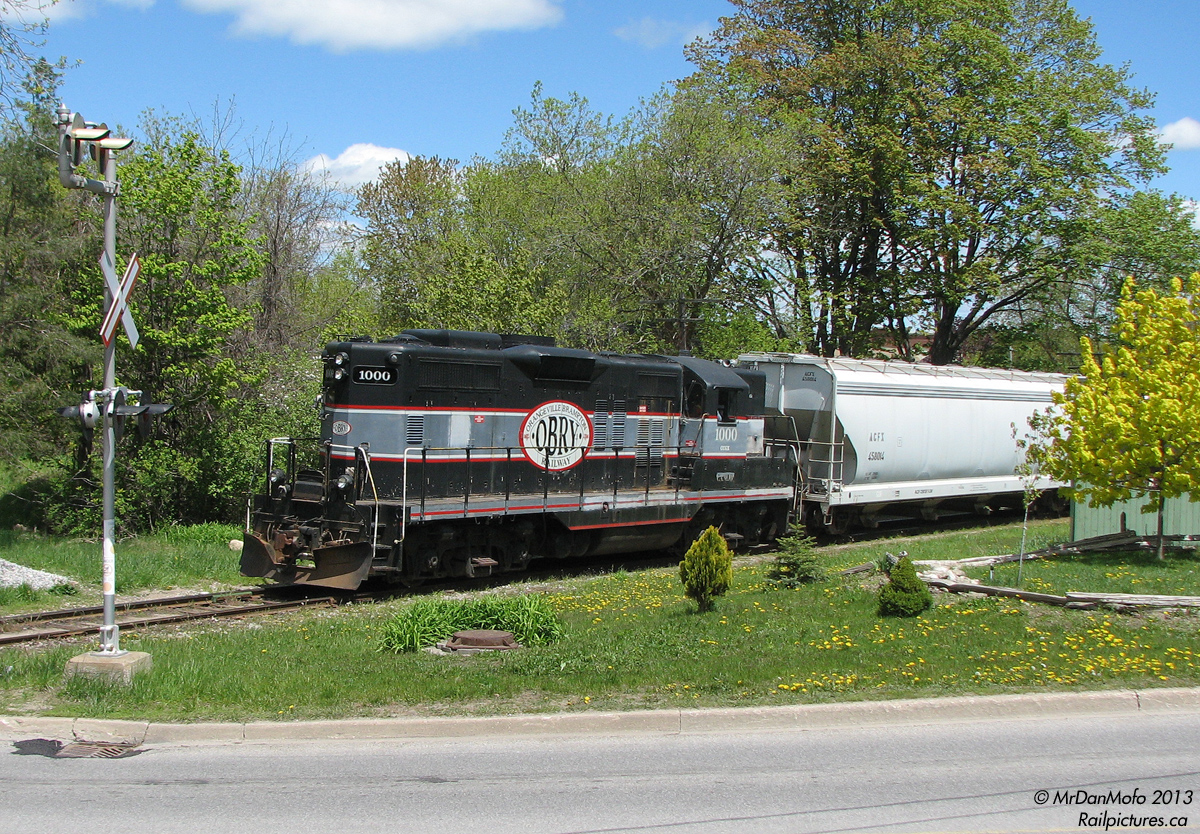 North Side Gal. While everyone always chases and photographs the Orangeville Brampton Railway's trip from Orangeville to Streetsville and back, there's another segment of the line less photographed.  On this day, after making the trip south to Streetsville and back, CCGX 1000 gathered some cars in the yard and left in the opposite direction of her arrival: north, to switch the few customers in the northern Orangeville industrial sector. Here we find the ol' gal, after spotting and lifting some cars, pushing her short train past the landscaped yards of quiet Orangeville neighbourhoods on the trip back to the yard.