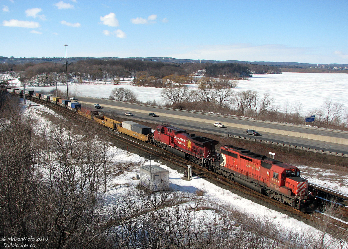 Heading north on the Canadian Pacific Hamilton Sub and about to begin the 18 mile ascent to Guelph Junction, an eastbound/northbound CP intermodal with CP 5941 leading 9813 (SD40-2/AC4400CW combo) heads through the plant at Desjardins, named after the Canal of the same name in the area, on a winter's mid-morn. A snow-covered Cootes Paradise is in the background under the blue sky, beyond the rail line and Highway 403.