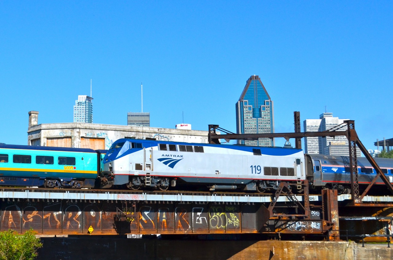 The outbound Amtrak Adirondack passes the inbound VIA Ocean/Chaleur about a mile south of Montreal's Central Station. They are passing the closed CN Wellington tower. Behind them is Montreal's skyline.