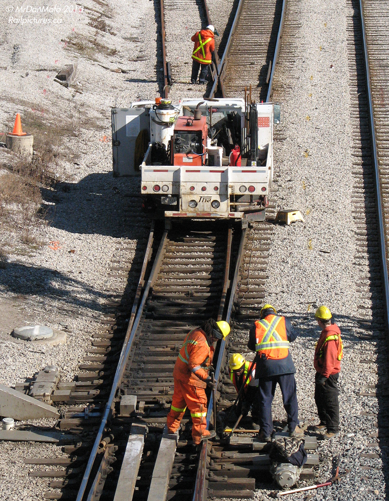 Maintenance is a part of the railway that many don't see, yet it serves a very important purpose: to keep the system in top-shape and in working order for safe passage of passengers and freight. During the afternoon lull in train traffic, a group of maintenance workers tend to one of the many switches at the east side of Bathurst Street. Four workers divert their attention to the area around the switch's points and heaters, while one is ahead at the "frog" where the diverging rail crosses. Their hi-rail truck sits nearby; well-stocked with tools, welding equipment and other items needed to make a quick spot repair or do one of the many regular maintenance tasks in the corridor.  Also of interest, note the VIA stepbox on the ground by the side of the truck, probably a spare "borrowed" from somewhere around Union Station.
