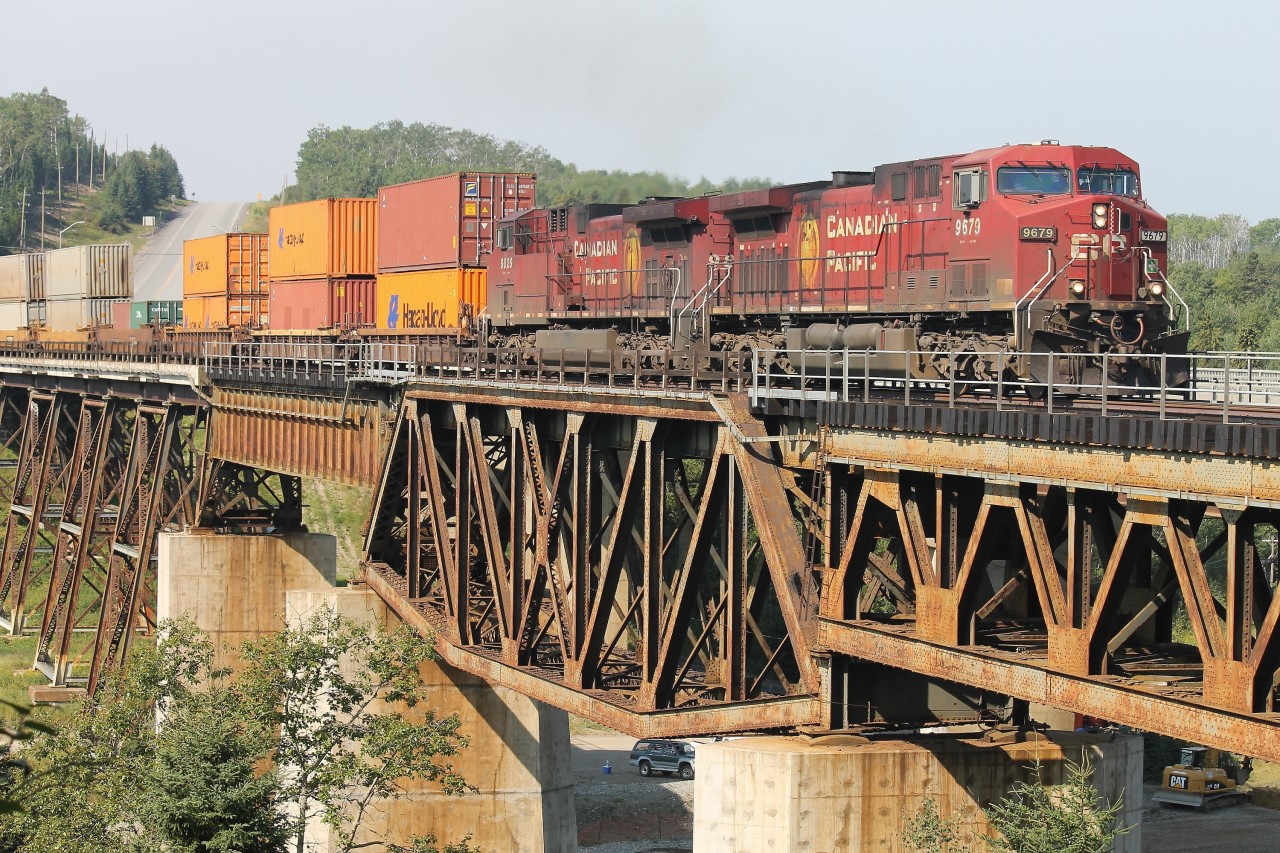 CP train 118 powered by a pair of GE’s - 9679 and 9829 - are almost across the Nipigon river on a combination of deck truss, plate girder and steel beam floor spans. On the north side of the railway and the highway structure [not visible] preliminary construction is underway for the first cable suspension highway bridge to be erected in Ontario.