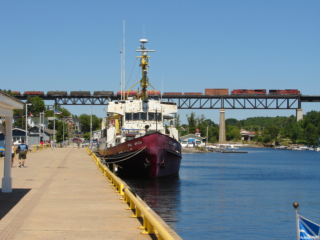CP 9571 South flying over the town of Parry Sound with train 220-13 from Thunder Bay to Toronto after lifting 8 cars at Nobel just north of town. Former Coast Guard ship "Still Watch", then known as the "Ville Marie" in the 80's, built by Russel Brothers Ltd. of Owen Sound in 1960 now calls Parry Sound home, after a lucrative career for the Canadian Coast Guard, several private owners, and at one point star of a Robert Ballard movie in 2002!