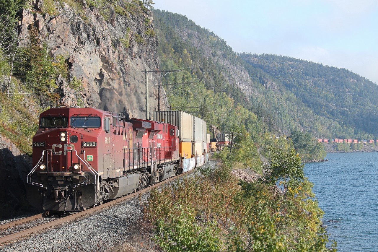 Train 113 led by CP 9623 and CP 8878 skirts along the shore of Lake Superior near Cavers. Rock slide detector fences are in place alongside the vertical rock faces where the first contractors blasted the roadbed out of the side of these cliffs.