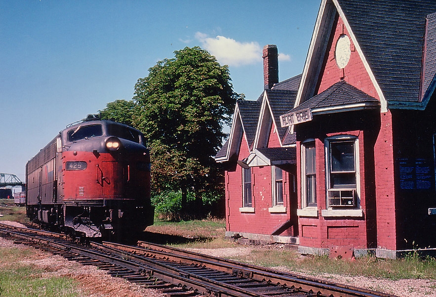 These were lean years for Amtrak. Dirty and sluggish, prone to failure, but still Amtrak carried on thru Niagara with what it could. Typical of the late 1970s before new F40PH locomotives were assigned to the Niagara run, these E9A locos, most built back in the 1950s, clattered along the line over the International Bridge to the USA before the route was changed and trains began crossing at Niagara Falls around early 1979.
In this view we have AMTK 425 and 409, it is about to cross to the USA after its station stop at the old flat roofed Fort Erie station which is out of sight behind the trees.  The former Bridgeburg station in the foreground was right next to the river crossing; some years ago it was relocated to the Fort Erie RR park on Central Ave.