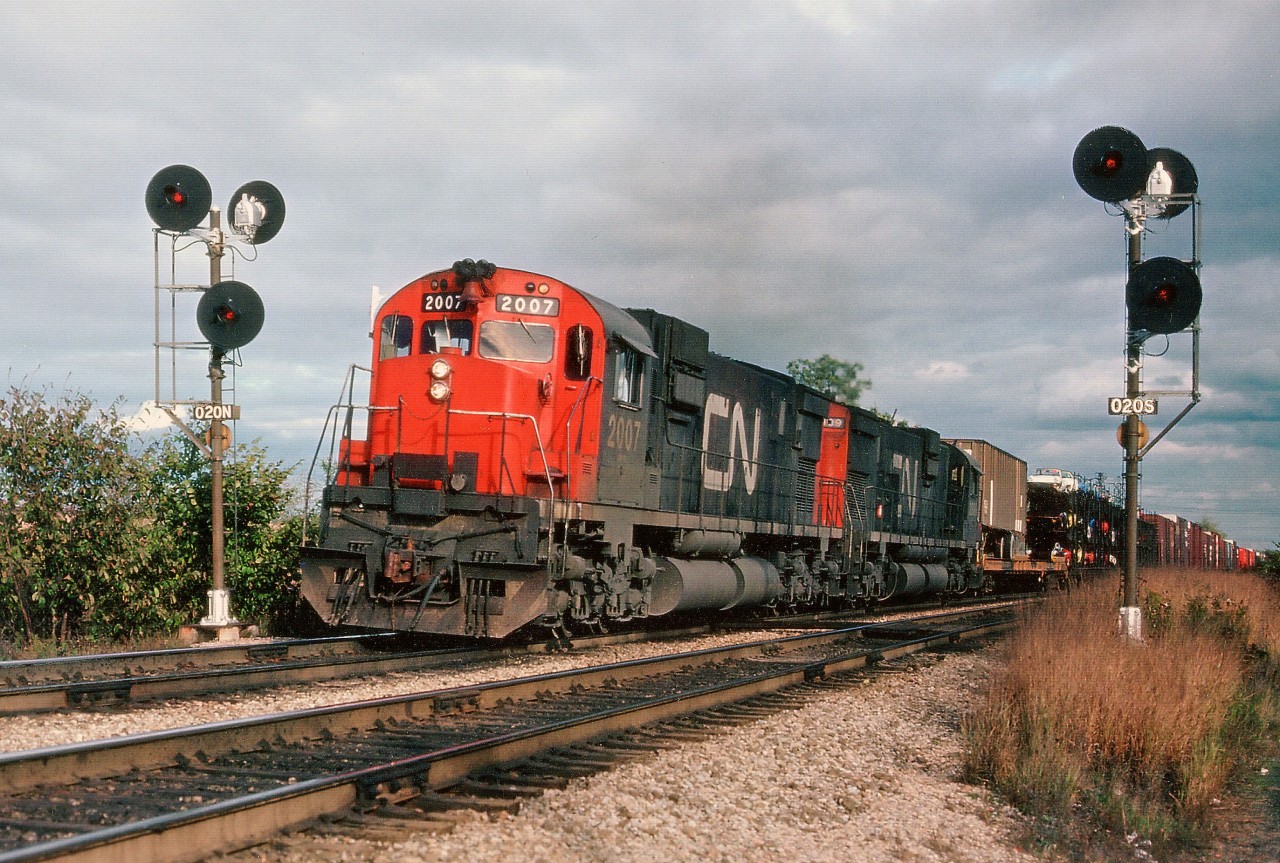 With the onslaught of GP40-2L(W)locomotives, of which more than 275 were on the scene by 1976, it was becoming increasingly difficult to catch CN trains powered by MLW C-630M diesels.  Pictured here are CN 2007, 2009 westbound thru the signals at Mile 2, Dundas, just before going over the York Rd bridge. Note open auto cars, and TOFC; both of which are never seen today. This is still a reasonable photo location, mid-afternoon and on.