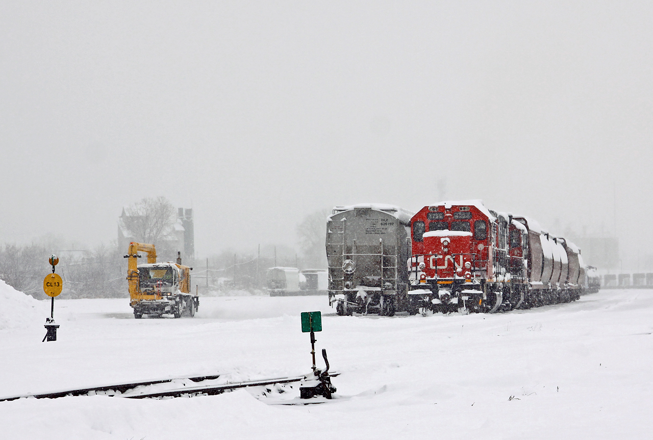 The snow let up temporarily as CN 511 hunkers down on track 13 in Racecourse yard while waiting for CN 509 and 439 to clear before running out to the grain elevator at Kerwood. Meanwhile, a super-duper hot air snowblower makes his way to the west end of the yard to clear some switches.