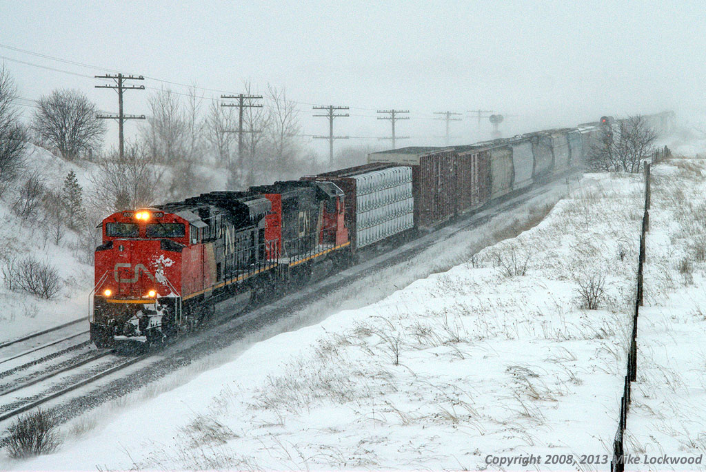 In the midst of a heavy snowstorm, CN 8006 and 5373 battle eastward with 320's train. Had it not been for the storm, the summit of the climb from Newcastle to Newtonville would almost be in sight, though calling it a summit is probably an overstatement as this is not exactly a legendary grade. It is, however, a slog for many an eastbound with the tendency of CN to assign just enough power to get over the road, not allow the engineer to exceed run 6 in order to conserve fuel, and even isolate a unit if it is deemed the train has an abundance of power. As I recall, this hogger was every bit of power that he could out of this pair; the whine of the turbo's being rather pronounced even with the snow deadening the sound. 1518hrs.