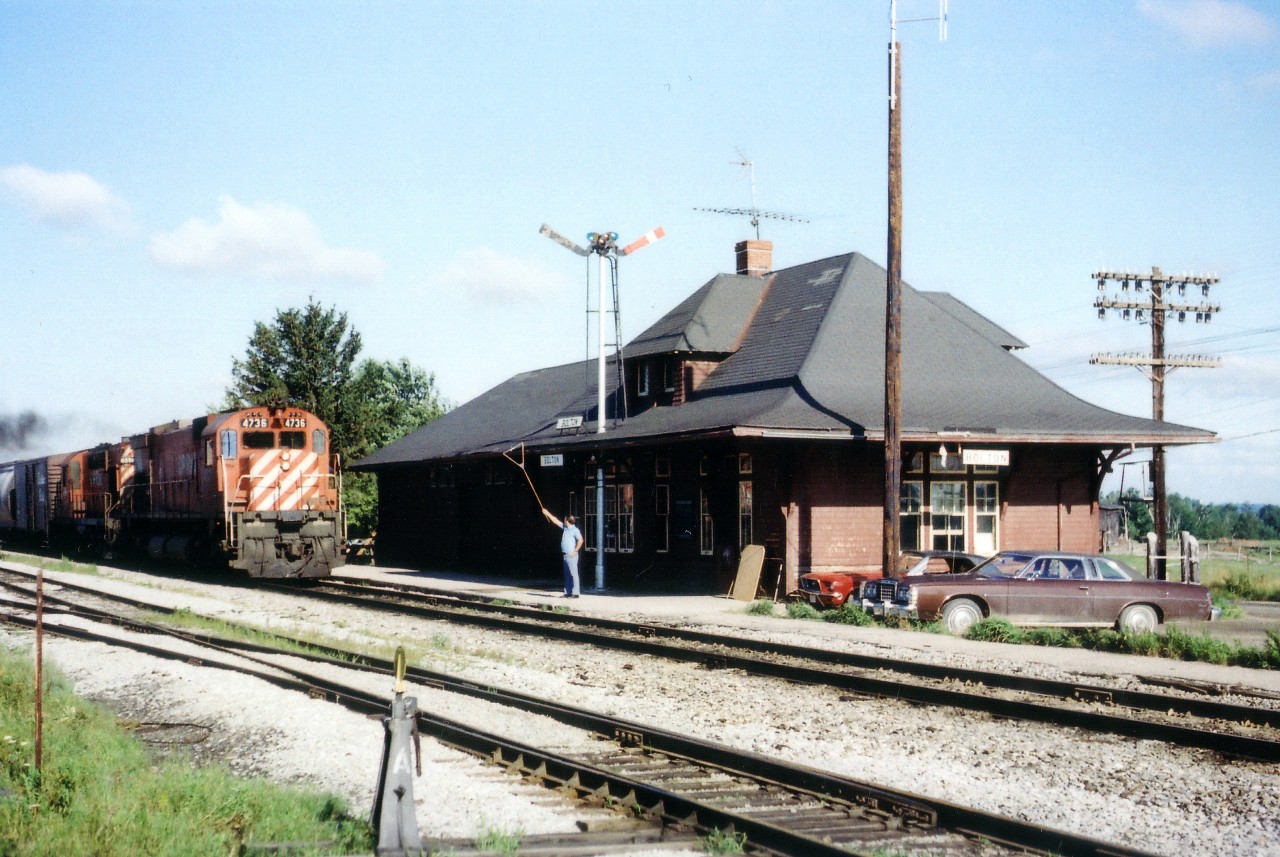 Orders on the Fly.......station agent at CP Bolton holds orders on the hoop for southbound CP 4736, 8594 as it roars past the depot. Station is long gone now, and I hope I have positioned its location correctly. Bolton is no longer the cowfield I remember it as. There is a story circulating amongst the older CP agents, most now retired, of a certain agent who was not very well liked. He worked out of a location currently popular with railbuffs. When he handed up the orders, the crewman would grab hoop and all, retrieve the flimsies off the hoop and throw the hoop where inclined, usually in a puddle or in the bush; causing the agent to go for a hike. It paid station personnel to keep the nose clean back then and NOT ruffle any feathers.......