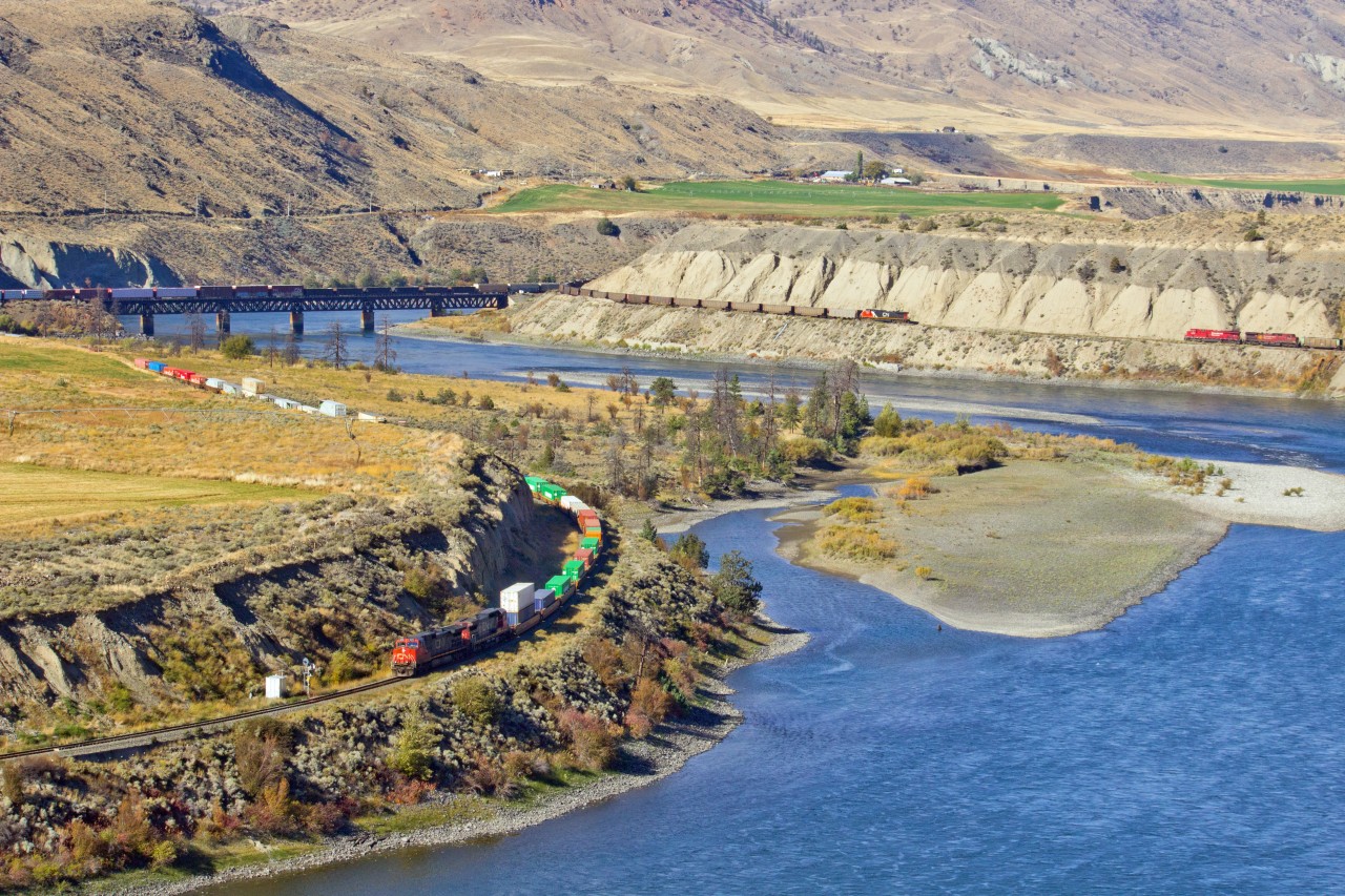 C.N.R. westbound on C.N.R. mainline on left.  C.N.R. with pusher and C.P.R. eastbound, stopped, on C.P.R. mainline on right.  On Thompson River about 2km. west of Basque siding and 10km. west of Ashcroft.  All trains run west on C.N.R and east on C.P.R. from Basque Siding to Mission, B.C.