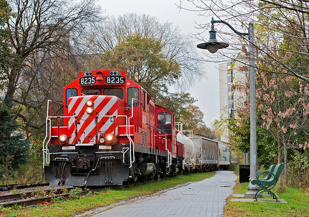 While everyone else talks about snow, it's a rainy autumn afternoon in Guelph. The daily Monday to Friday roadswitcher out of Guelph Jct is seen heading back south to finish off PDI Elizabeth St and the Liquid Yard after switching AOC Canada on the South Industrial and lifting the interchange which consisted off two hydrochloric acid tank cars (PDI Liquid Yard), a plastic hopper (PDI Elizabeth St) and a lime hopper (Owens-Corning Fiberglas) from the GEXR. The trail I'm standing on to get this photograph is the old CPR mainline which was torn up to make way for the trail, the train is on the old siding which is now the new mainline.