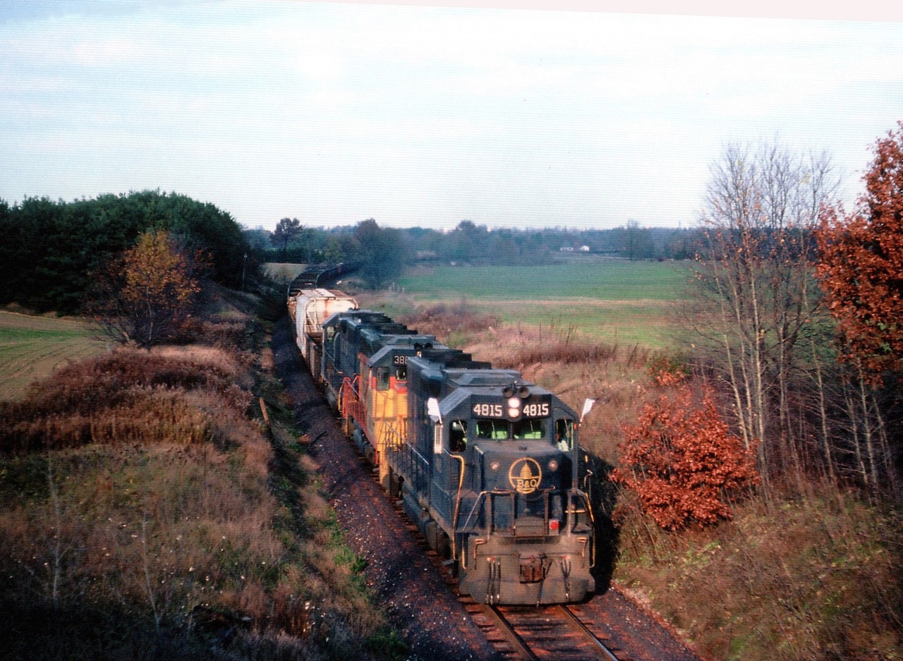 The FIRST of the dedicated TH&B steel slab trains from Hamilton (Stelco) to Nanticoke is shown here, about to roll under Cty road 4 on the late afternoon of November 7, 1983. The train reached Nanticoke initially by way of TH&B to x-LE&N at Waterford, down to Simcoe, onto CN, thru Renton & Jarvis to Nanticoke's own trackage. CP purchased some RoW and was then able to reroute these trains along the CASO at Waterford and then on to Jarvis.
Shown here are B&0 4815,C&O 3885 and 4828, power brought in for startup. This train, with the usual 20 cars of 80 tons of slabs each proved to be a real moneymaker until track patrol on May 20, 1986 found a mud-slide beginning at the Cainsville Fill after heavy rain. That night, thousands of tones of fill slid down into the Grand River, and that was the end of the line for the TH&B in this area. Rerouting from Hamilton to Welland and west on the CASO proved to be too costly, as a result the job was handed over to CN. The steel contract was initially broken into 10 week periods, with CN running trains 6 of 10 weeks, and TH&B the other 4. Soon CN took over completely, and the Hamilton to Brantford/Waterford line was abandoned May 2, 1989, and tracks pulled up that same year.