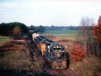 The FIRST of the dedicated TH&B steel slab trains from Hamilton (Stelco) to Nanticoke is shown here, about to roll under Cty road 4 on the late afternoon of November 7, 1983. The train reached Nanticoke initially by way of TH&B to x-LE&N at Waterford, down to Simcoe, onto CN, thru Renton & Jarvis to Nanticoke's own trackage. CP purchased some RoW and was then able to reroute these trains along the CASO at Waterford and then on to Jarvis.
Shown here are B&0 4815,C&O 3885 and 4828, power brought in for startup. This train, with the usual 20 cars of 80 tons of slabs each proved to be a real moneymaker until track patrol on May 20, 1986 found a mud-slide beginning at the Cainsville Fill after heavy rain. That night, thousands of tones of fill slid down into the Grand River, and that was the end of the line for the TH&B in this area. Rerouting from Hamilton to Welland and west on the CASO proved to be too costly, as a result the job was handed over to CN. The steel contract was initially broken into 10 week periods, with CN running trains 6 of 10 weeks, and TH&B the other 4. Soon CN took over completely, and the Hamilton to Brantford/Waterford line was abandoned May 2, 1989, and tracks pulled up that same year.