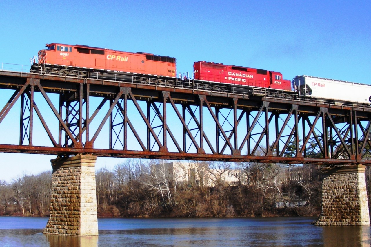 Westbound hopper train crosses the Grand River after stopping at Galt station. Viewed from the west river bank in Riverbluff Park.