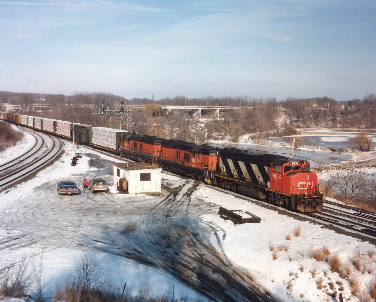 For a brief period in & around 1988 the CN had on lease five B&LE SD9s, numbers 825,827,829,841 and 843. Here we see CN 9636, B&LE 825 and 841 on a Fort Erie-bound train rumbling thru Bayview Jct. on a 'not bad' for winter February afternoon. In the photo between his car (right) and mine (left) is rail buff Pete Hoople, keeping an eye on his video camera as the train passes. In the centre on the horizon is the lone smokestack for the defunct Burlington Brick Plant, a business since razed and replaced with a housing survey. Now "Off Limits" is this location known for us being able to sit in our cars, keep warm, and listen to the scanner while eyeing the signals. Railfanning at its laziest. :o)