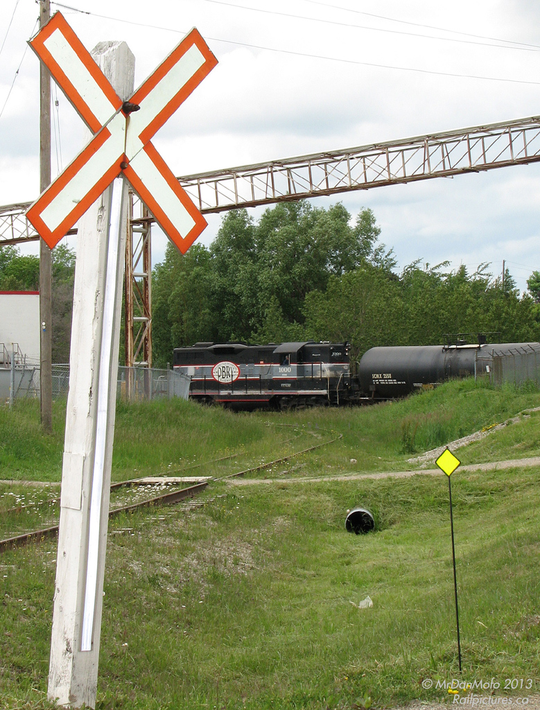 Working the north end of Orangeville (south of where the line to Owen Sound ends and was ripped up by the CPR), Orangeville Brampton Railway's once sole power CCGX 1000 switches tanks at PolyOne Canada, one of the few industries on the OBRY. The crossbucks mark a road crossing of the spur pictured, that once lead to customers in another industrial area.  The 36 mile rail line was purchased by the Town of Orangeville in 2000 when the CPR was about to abandon it (and subsequently rip the rest of it up), which would have impacted a number of industries and jobs in Orangeville that relied on the railway as a competitive means to ship their products. Since day one, Cando Contracting has operated the line for the town, which includes supplying their own power and switching out the roughly half-dozen customers in Brampton and Orangeville on a biweekly (twice a week) basis.