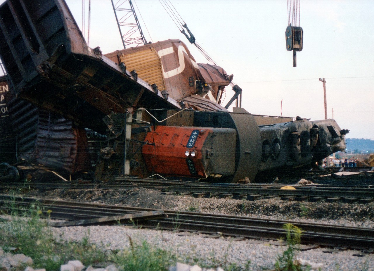 An image such as this brings the real meaning out "She was as ugly as a train wreck" because major wrecks really can be a mess. But, unfortunately, they are a fact of railroading.
On August 5, 1978 CN's #387 was Hamilton-bound from Niagara when it hit an open switch. CN 9404, 4523, 4524 and 4573 piled up along with a considerable number of cars. This image is from August 7th, as late day spectators (a line in the background on the right)watch the cleanup in progress. Track in foreground was once part of the line that ran over the Burlington Beach strip. It was severed when the S.Ck traffic circle on the QEW was removed back in the 1970s.
As much as Lac Megantic has been at the front of the railroad news this year, I feel there were a lot more derailments in the past. In a short stretch I recall major ones at Simcoe, at CN Robbins, at Grimsby, Aldershot and Burlington. No, they did not all get a visit from me.
This derailment was blamed on vandals cutting into the lock at the switch, mile 37.6 Grimsby Sub.